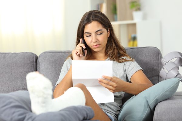 Woman with a broken foot on the phone while looking at a letter that was sent to her as a common auto insurance company delay tactics